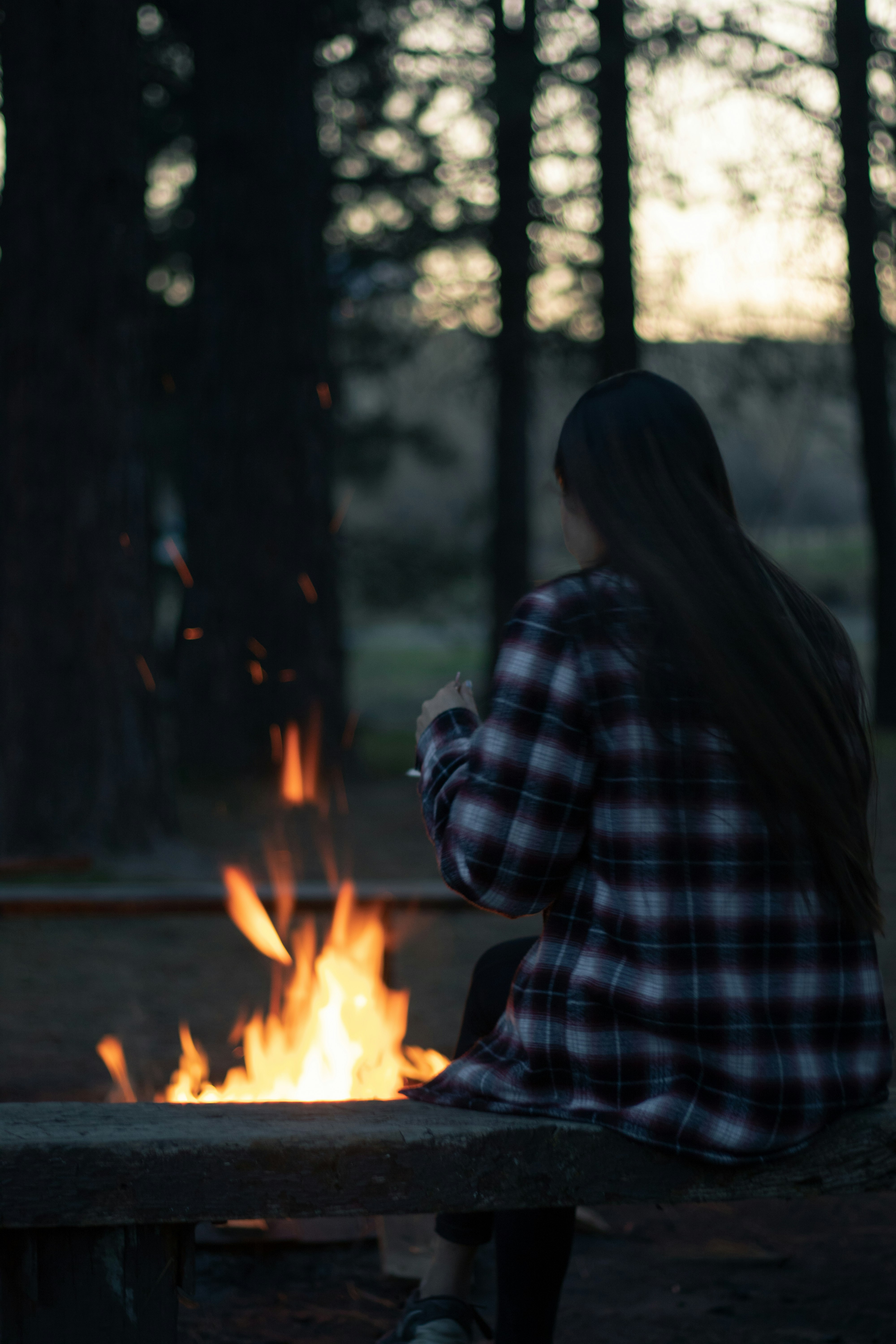 woman in blue and white plaid dress shirt standing near bonfire during daytime